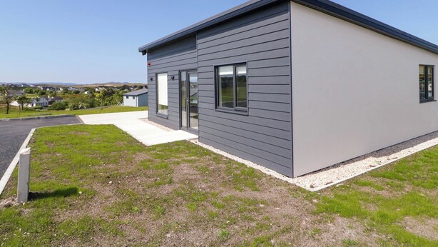 A modern single-story building with a flat roof, large windows, and a concrete driveway. - Number 3 Villa - The View (Bunbeg)