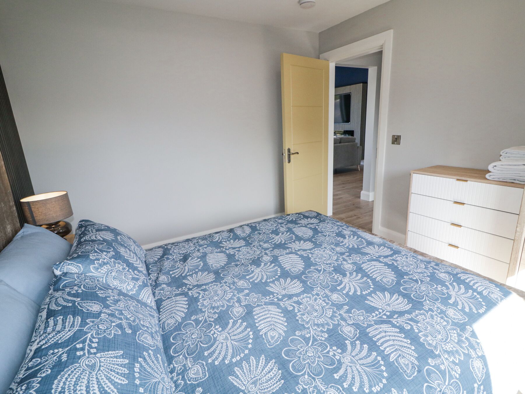 Ein Schlafzimmer mit einem Bett, einer Nachttischlampe, einem Schminktisch und einer Tür zu einem anderen Raum.
