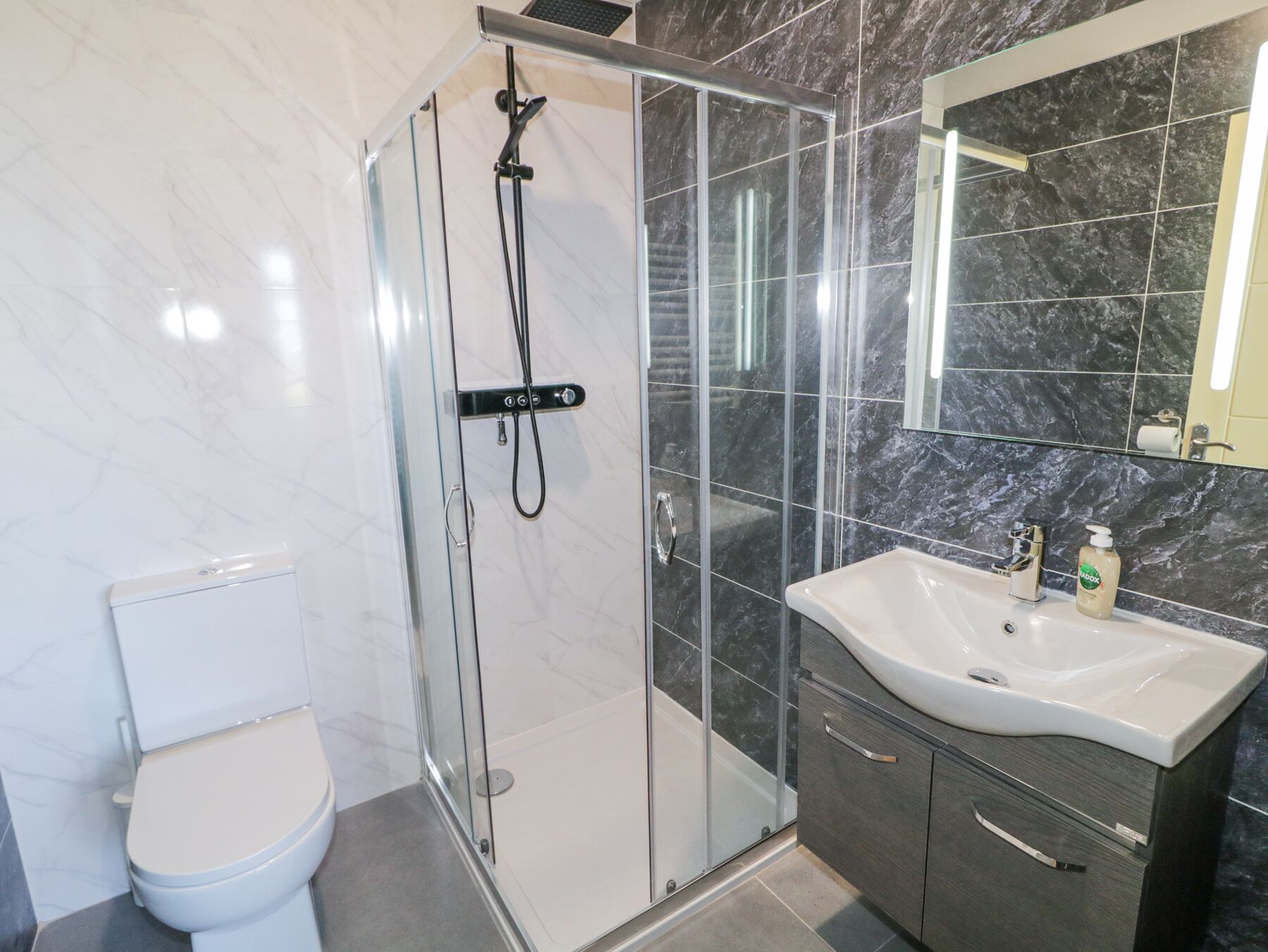 A modern bathroom with a glass-enclosed shower, a white toilet, a sink with a mirror, and dark marble tiles.