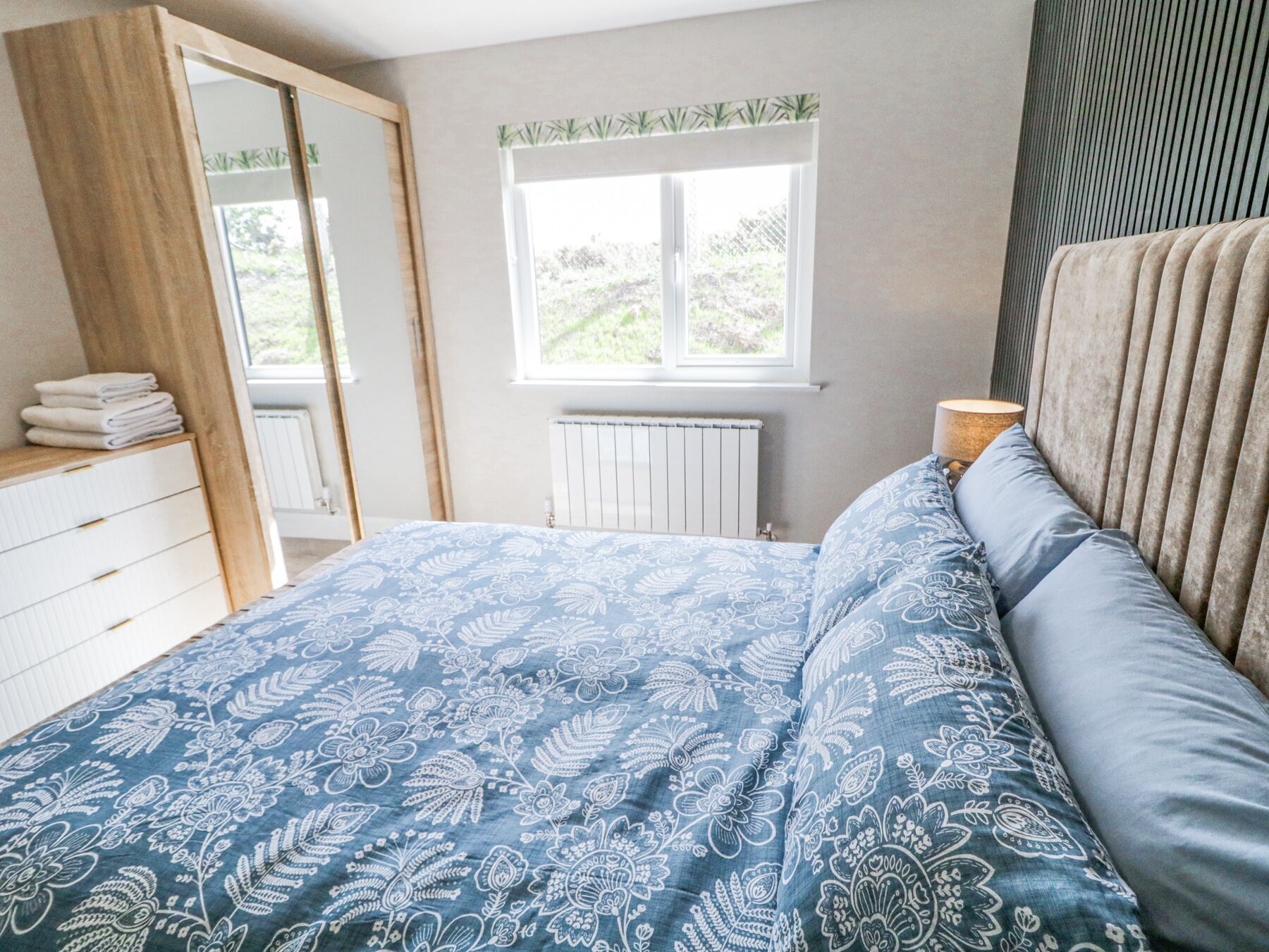 Un dormitorio con cama, cómoda, ventana y radiador.