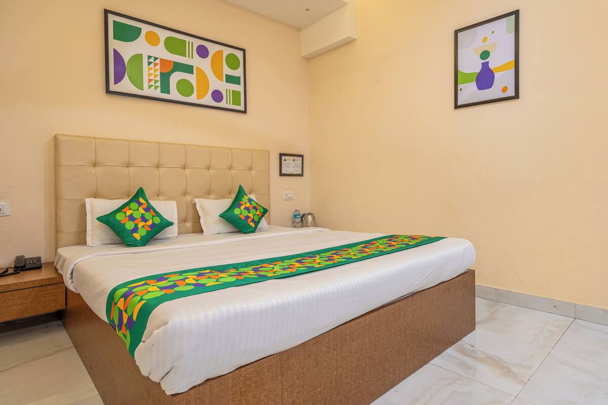 Una habitación de hotel con una cama grande, dos almohadas, una mesita de noche y dos cuadros enmarcados en la pared.