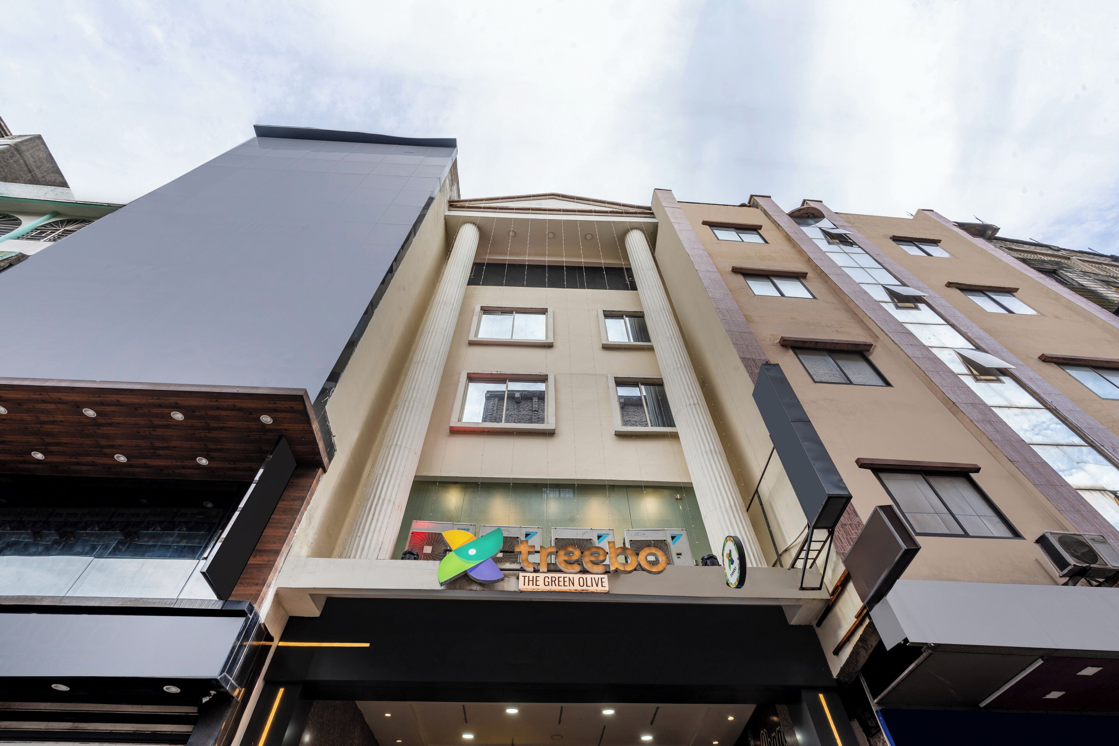 Un edificio de varios pisos con fachada moderna, ventanas amplias y un letrero del restaurante 'The Green Olive'.
