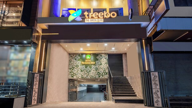 Exterior do Hotel The Green Olive, com fachada moderna, escadaria para a entrada e área de estacionamento visível.