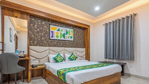 Quarto com estrutura de cama de madeira, escrivaninha com cadeira, mesa de cabeceira e uma janela grande com cortinas.