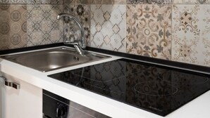 Una cocina con estufa negra, pileta de acero inoxidable y azulejos decorativos en la pared.