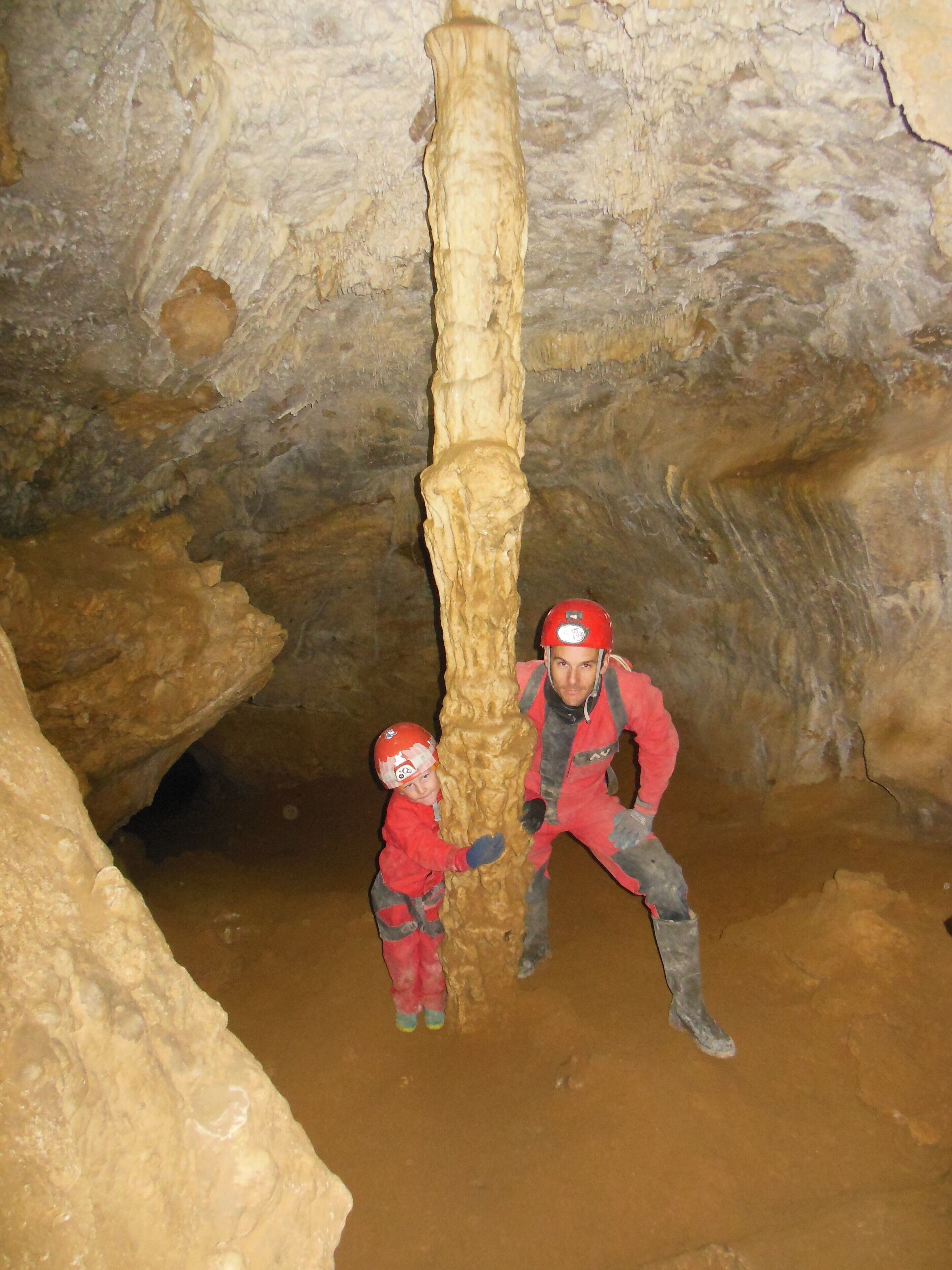 Two people in a cave with a large stalactite formation.