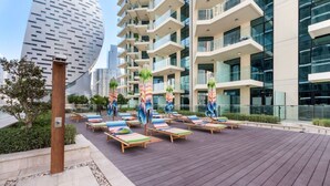 A rooftop lounge area with sun loungers and umbrellas, surrounded by modern buildings. - Missoni | Canal View | Fully Furnished Studio (Dubai)