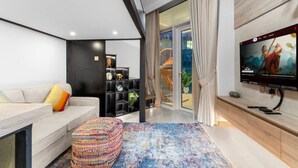A modern living room with a sofa, a colorful ottoman, a black shelving unit, a TV, and a sliding glass door leading to a balcony. - Missoni | Canal View | Fully Furnished Studio (Dubai)