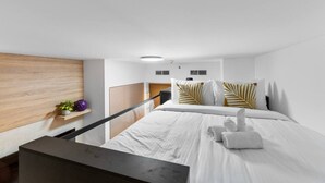 A modern hotel room with a bed, a wooden headboard, a small shelf with plants, and a black desk. - Missoni | Canal View | Fully Furnished Studio (Dubai)