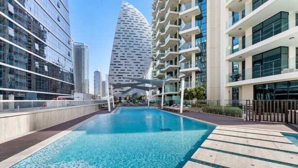 A modern hotel with a rooftop pool, surrounded by high-rise buildings and a distinctive tower in the background. - Missoni | Canal View | Fully Furnished Studio (Dubai)