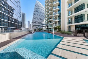 A modern hotel with a rooftop pool, surrounded by high-rise buildings and a distinctive tower in the background.