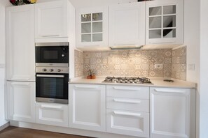 Una cocina con armarios blancos, horno integrado, microondas y estufa a gas.