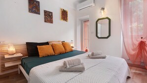 A bedroom with a bed, pillows, a bedside table with a lamp, artwork on the wall, and an air conditioning unit. - Apartment 'Giada's Retreat' with Sea View, Wi-Fi and Air Conditioning (Genova)