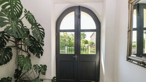 Una puerta negra con marco blanco, una planta grande en maceta a la izquierda y un espejo en la pared a la derecha.