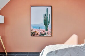 Une chambre à coucher avec un lit, un tableau encadré représentant un cactus et un plancher en bois.