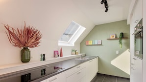 A modern kitchen with a skylight, white cabinets, a black countertop, and a green vase with dried plants. - Spacious 3 bedroom apartment with parking (Machelen)