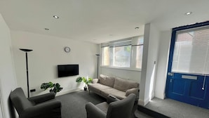 A living room with a sofa, two armchairs, a flat-screen TV, a floor lamp, and a potted plant. - Spacious 4-bedroom House - Garden & Free Parking (Faversham)