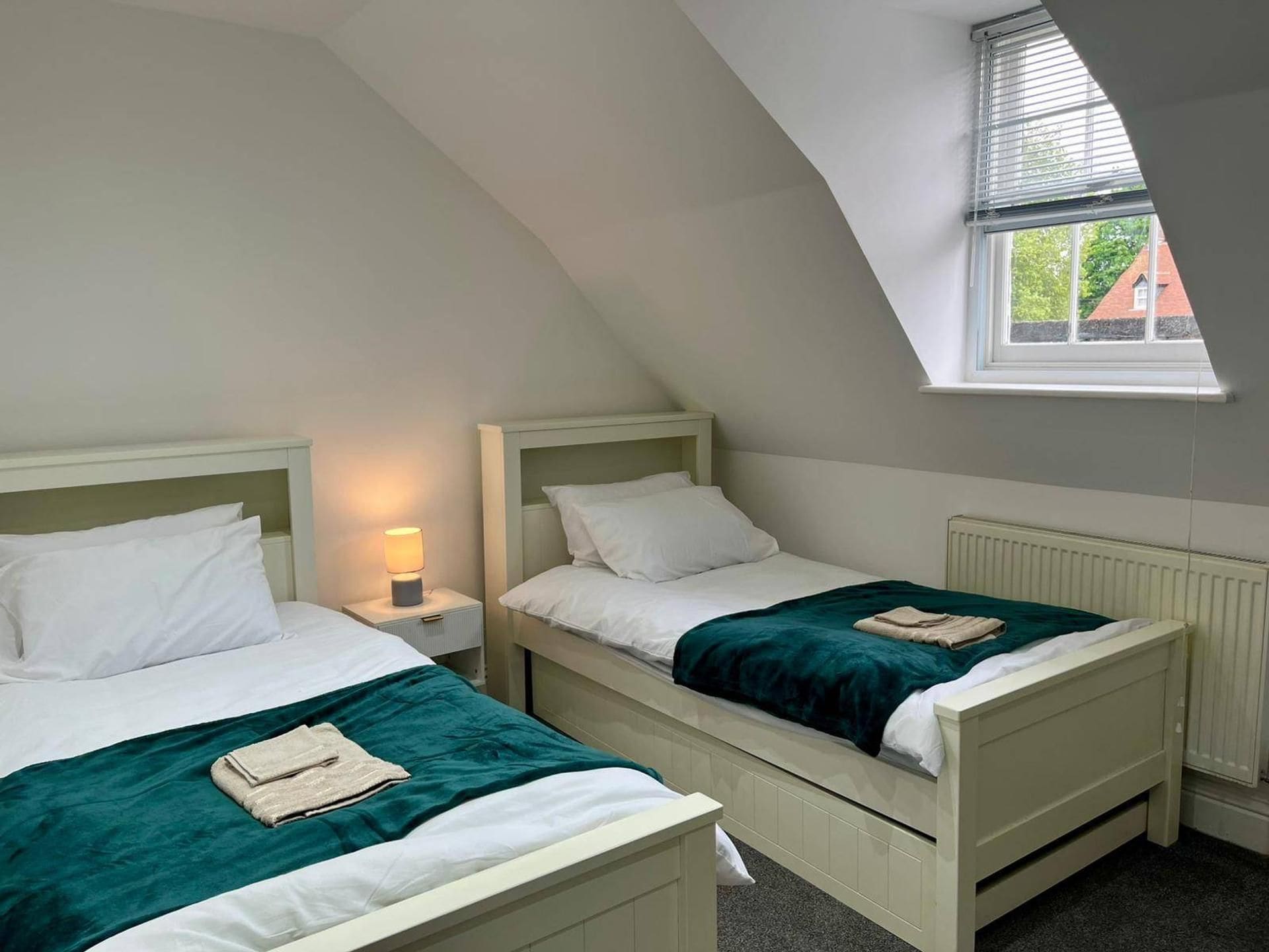 A room with two beds, a window, and a radiator.