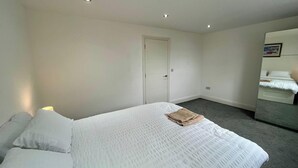 A hotel room with a bed, a bedside table, a mirror, and a door. - Spacious 4-bedroom House - Garden & Free Parking (Faversham)
