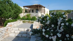 Ein Gebäude mit Steinsäulen und einer Holzpergola, eine Steintreppe und weiße Blumen.