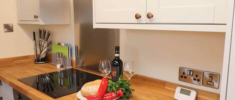 A kitchen with a wooden countertop, a bread roll, red peppers, a bottle of wine, and a wine glass.