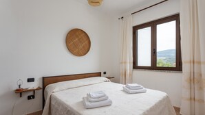 A bedroom with a bed, a window with curtains, a wall-mounted basket, and a bedside table with a lamp. - Holiday Home 'Santa Caterina' with Mountain View, Wi-Fi and Air Conditioning (Santa Caterina di Pittinuri)