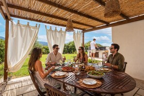 A covered outdoor dining area with a table set for four people, surrounded by greenery and a view of the landscape. - Holiday Home 'Santa Caterina' with Mountain View, Wi-Fi and Air Conditioning (Santa Caterina di Pittinuri)