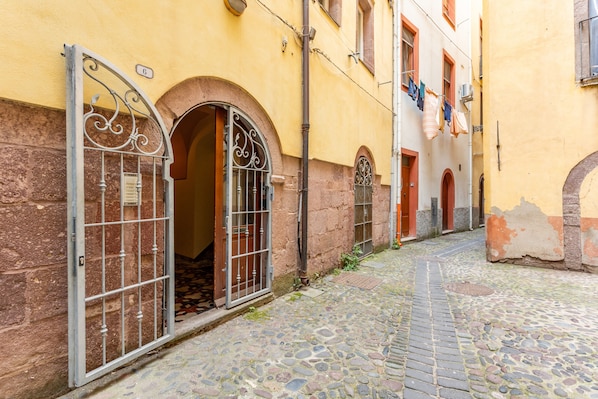 A cobblestone street with a yellow building, an open metal gate, and a clothesline with garments.