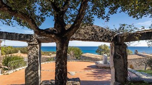 Un espace extérieur agrémenté de structures en pierre, d’un arbre et offrant une vue sur la mer.