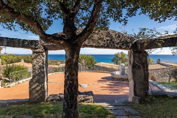 An outdoor area with stone structures, a tree, and a view of the sea.