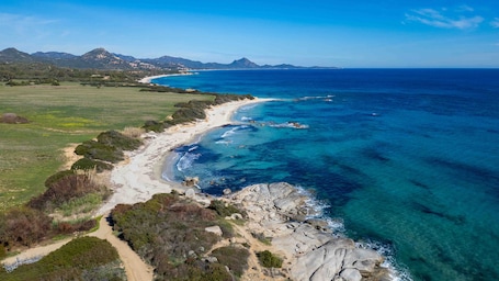A coastal landscape with a beach, clear blue waters, and distant mountains.