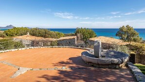 Une cour avec une fontaine en pierre, une terrasse circulaire en briques et une vue sur la mer.