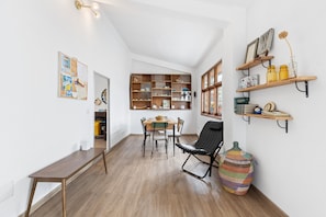 Une pièce comprenant une table à manger en bois, des chaises, un fauteuil noir, une bibliothèque et un grand panier en osier.