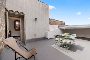 Un balcon avec une table et des chaises, un fauteuil en osier et une porte donnant sur un espace intérieur.