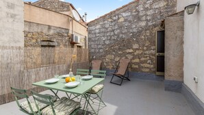 Un patio con una mesa lista para dos personas, sillas y una pared de piedra al fondo.