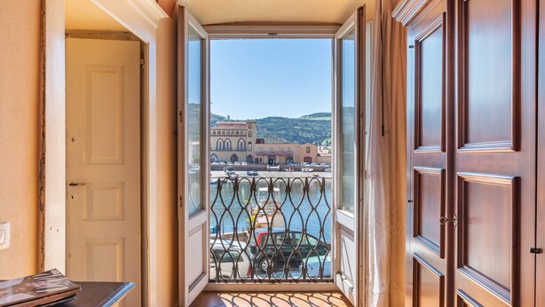 Ein schmaler Gang führt zu einem Balkon mit Blick auf einen Jachthafen und Gebäude.