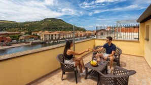 A balcony with two chairs, a table, and a view of a river and buildings.