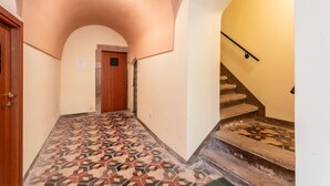 A hallway with patterned flooring, a wooden door, a staircase with a handrail, and a ceiling light.