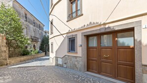 Une ruelle étroite pavée, bordée d’un bâtiment qui se distingue par une grande porte en bois et un mur de pierre.