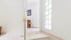 Un couloir avec un mur blanc, une porte, un tableau encadré et une fenêtre avec du verre teinté de vert.