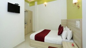 Un dormitorio con cama, mesita de noche y televisor montado en la pared.