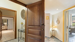 A wooden door, a round woven wall decoration, a small table with a lamp, and a tiled floor. - Apartment 'La Residenza Color Del Mare' with Balcony, Wi-Fi and Air Conditioning (Bosa)