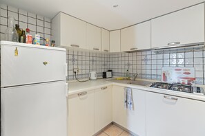 Una cocina con armarios blancos, un refrigerador, una estufa y varios utensilios de cocina sobre la encimera.
