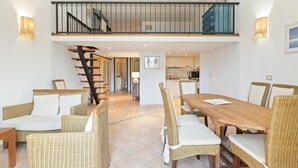 A spacious dining area with wicker furniture, a staircase leading to a balcony, and a kitchen in the background. - Apartment 'La Residenza Color Del Mare' with Balcony, Wi-Fi and Air Conditioning (Bosa)