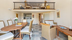 A dining area with a wooden table, wicker chairs, and a balcony with wicker furniture.