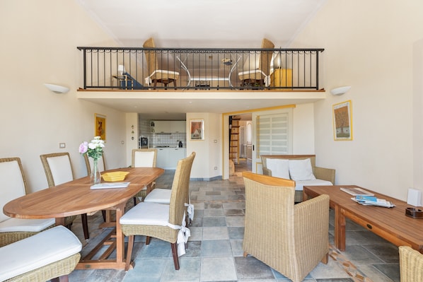 A dining area with a wooden table, wicker chairs, and a balcony with wicker furniture.