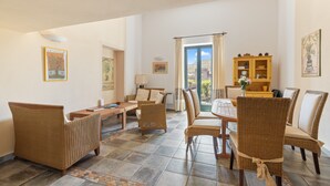 A spacious living area with wicker furniture, a dining table, and a view through a glass door.