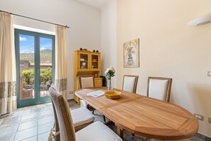 A dining area with a wooden table, chairs, a yellow cabinet, and a view through a glass door.