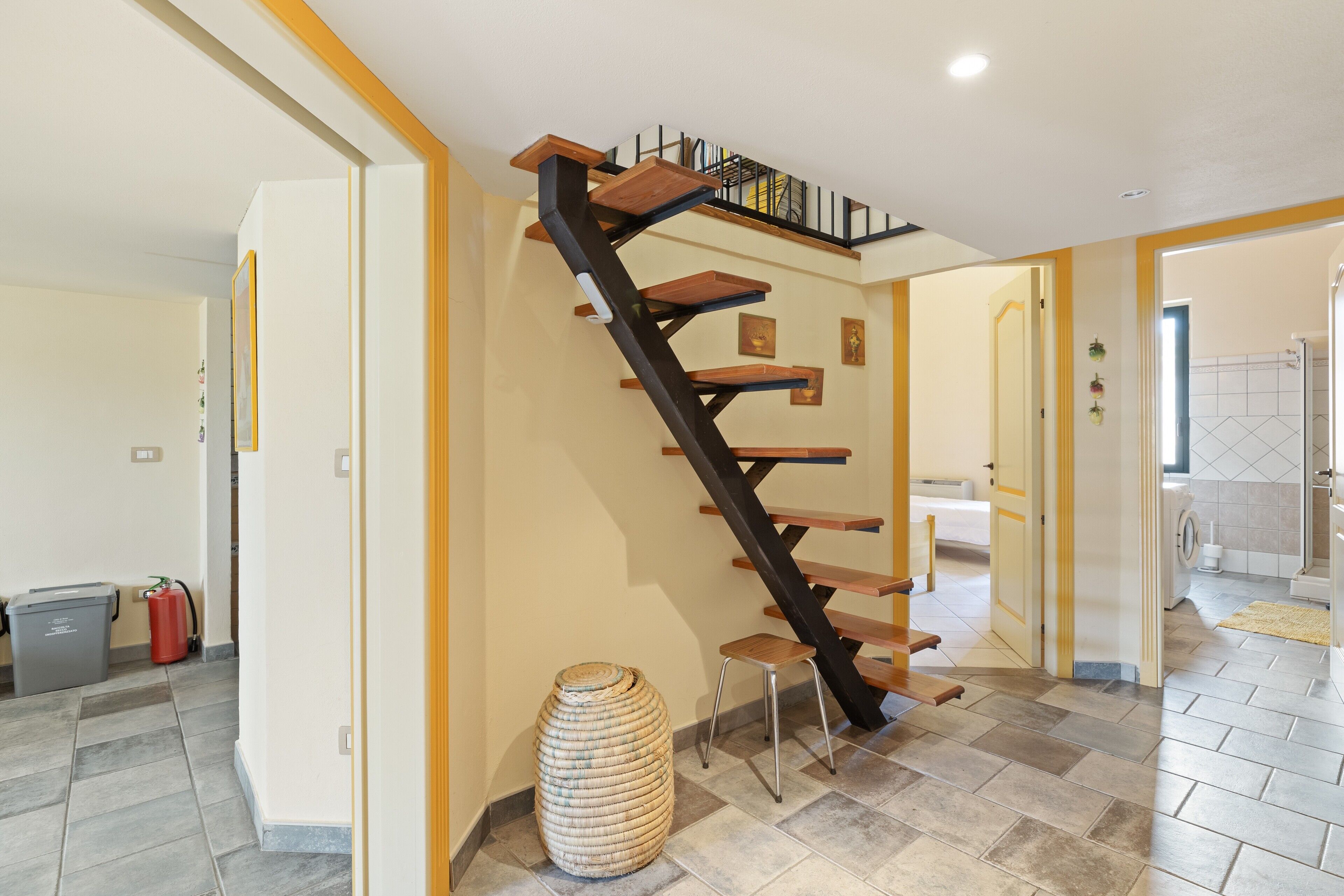 A staircase with wooden steps and black railings, leading to a landing with a bookshelf.