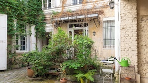 A courtyard with potted plants, a white table, and a green watering can.